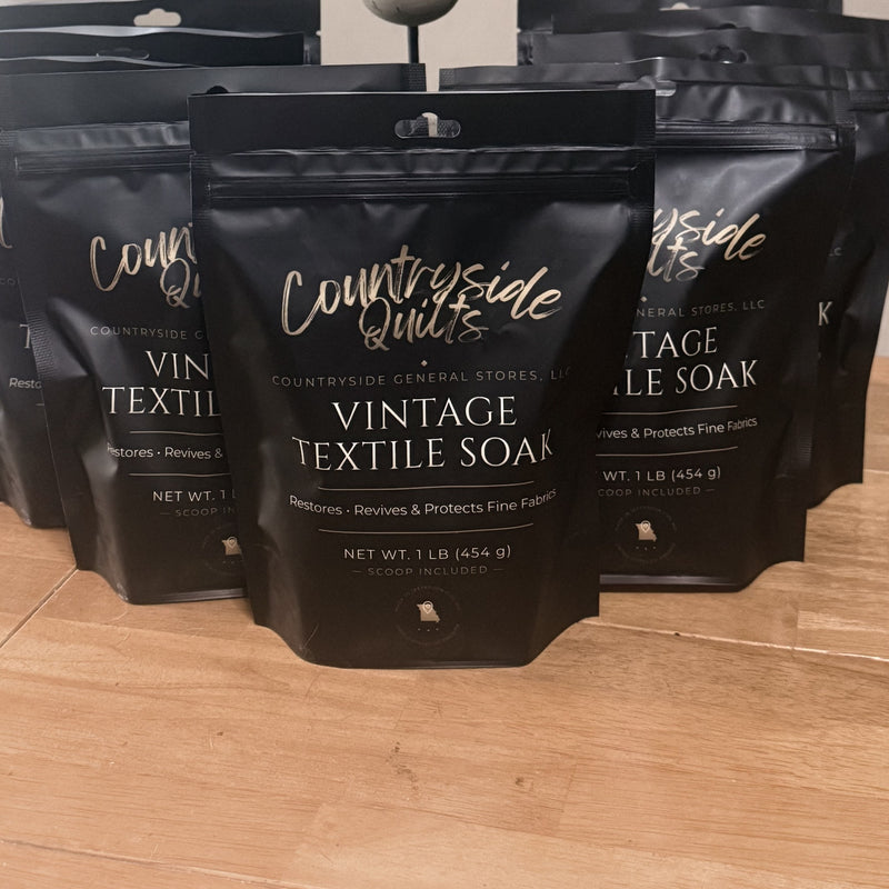 One pound pouches of Countryside Quilts Vintage Textile Soak, matte black with gold lettering, on a wooden table